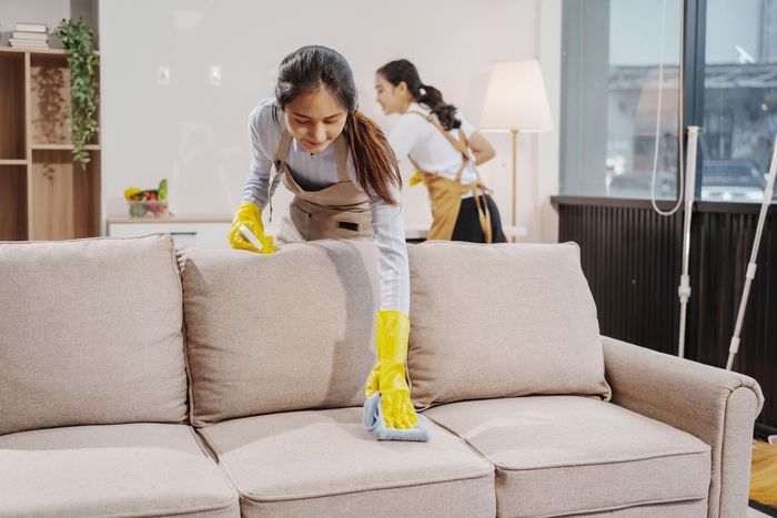 A woman in yellow gloves is cleaning a beige sofa A woman in yellow gloves is cleaning a beige sofa