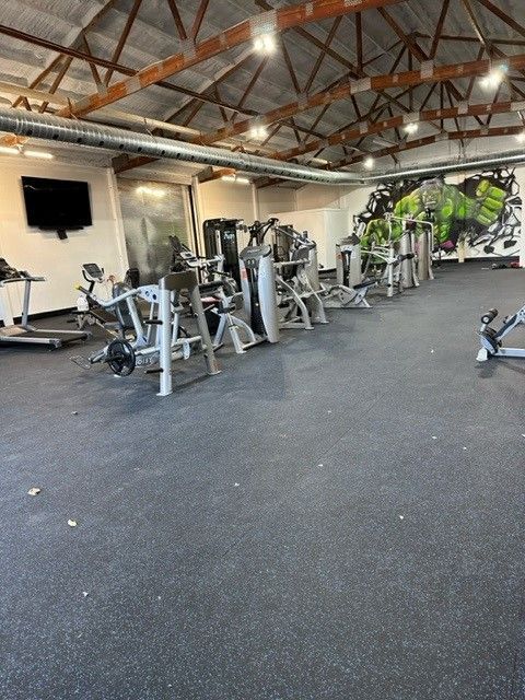 Gym interior with weight machines, black floor, and a Hulk mural on the wall