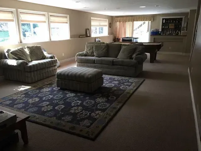 Living room with sofa, armchair, ottoman, rug, pool table, and bar