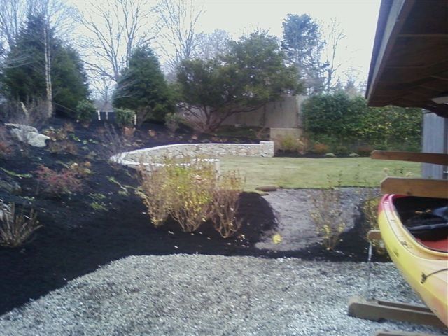 Backyard garden with gravel path, lawn, shrubs, and a yellow kayak at the right edge