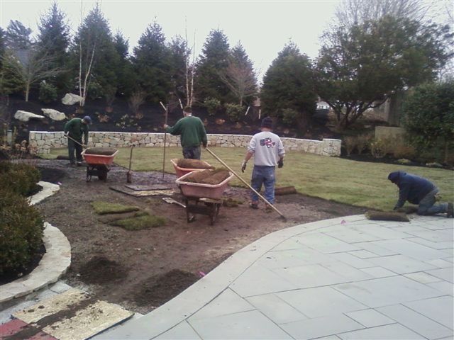 Workers shoveling and leveling soil in a landscaped garden beside a paved walkway