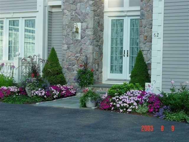 Front entrance with stone facade, glass doors, and flower beds along a driveway