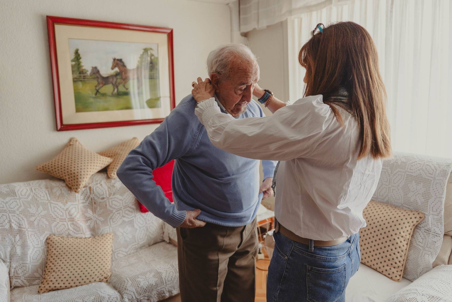Woman helping an older man put on a sweater, illustrating signs a parent may need assisted living.