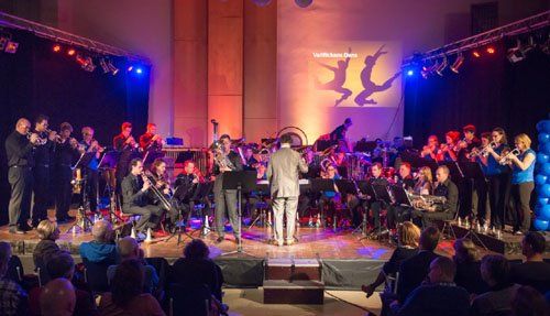Orkest en koor treden op op een podium met kleurrijke verlichting en een dirigent in het midden.