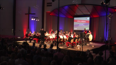 Het orkest treedt op op een schemerig verlicht podium met rode verlichting en een projectiescherm achter zich.