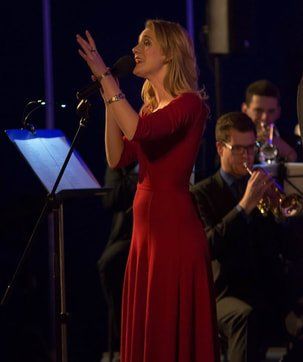 Zangeres in een rode jurk treedt op het podium op, met muzikanten op de achtergrond.