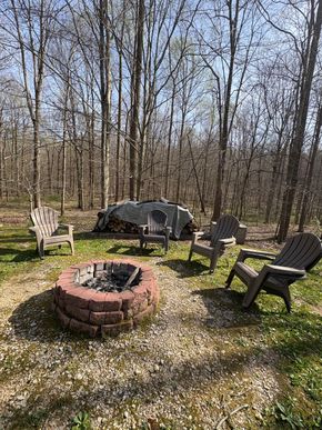 Backyard fire pit with four chairs, one covered grill, and a wooded backdrop