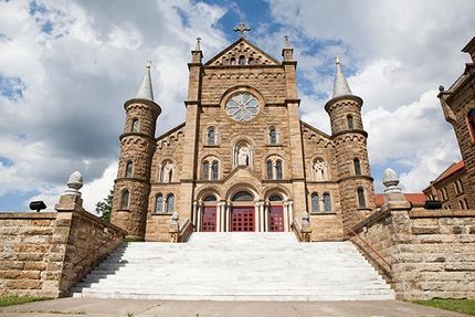 Stone church with twin towers and red doors at the top of wide white steps under a cloudy sky