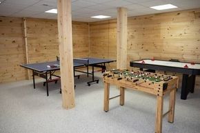 Basement recreation room with ping-pong and foosball tables under exposed wood beams