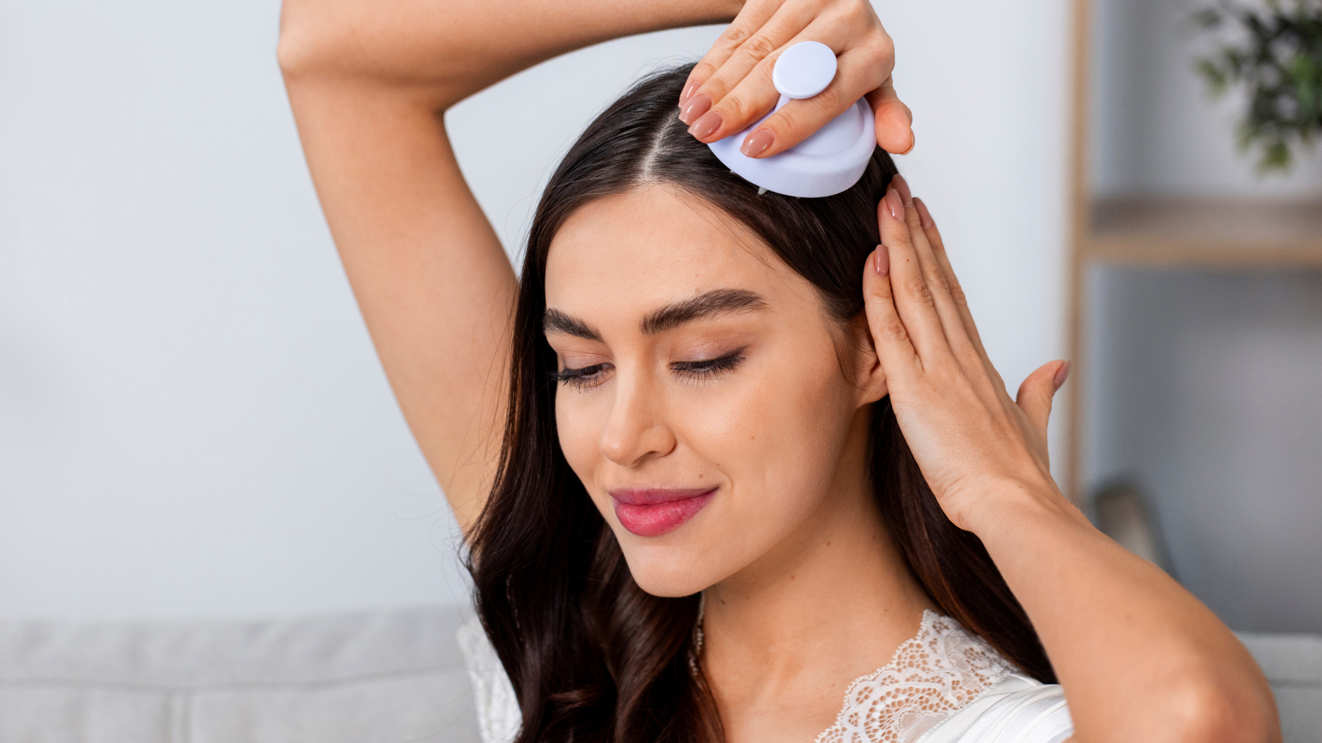 Woman using a scalp massager, eyes closed, indoors.