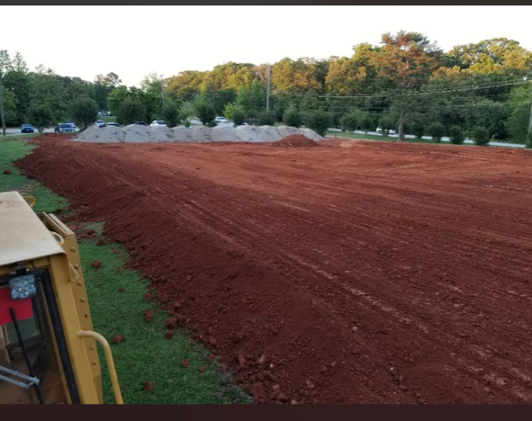 A bulldozer is moving dirt in a field with trees in the background.