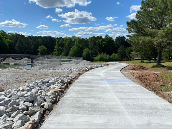 A concrete walkway going through a forest with rocks on the side.