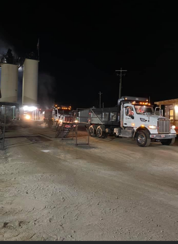 A dump truck is parked in a dirt lot at night.