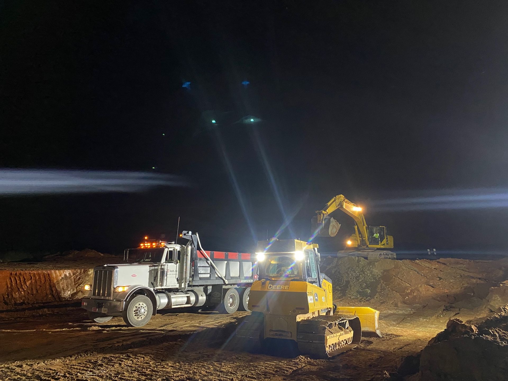 A dump truck is being loaded with dirt by a bulldozer at night.