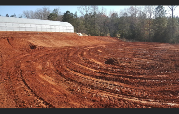 A large dirt field with a greenhouse in the background.