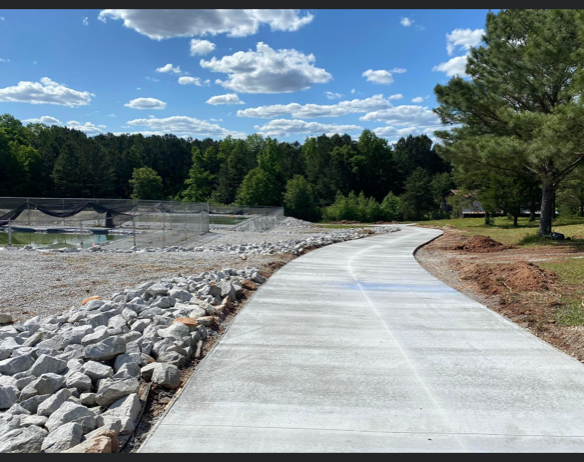 A concrete walkway going through a park with trees and rocks on the side.