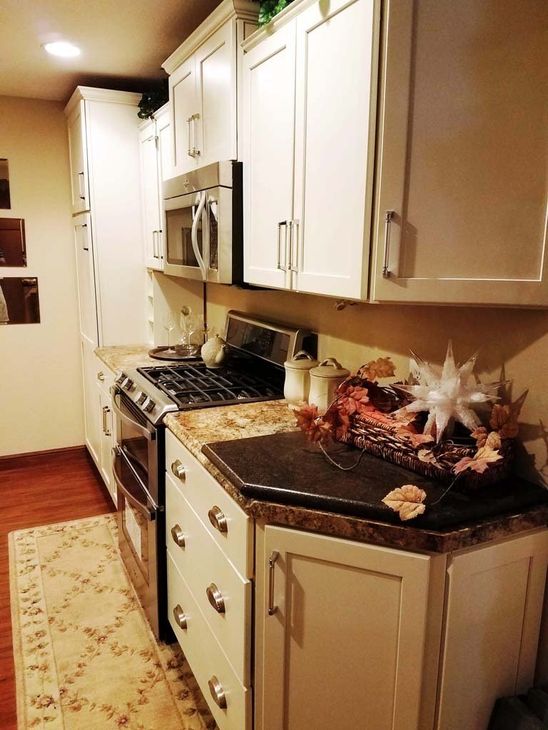 White kitchen with stainless steel appliances, wooden floors, and countertop decorations.