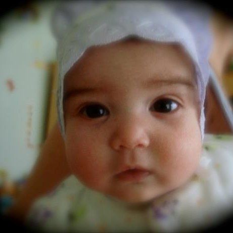 Baby with big brown eyes wearing a white bonnet, looking directly at the camera.