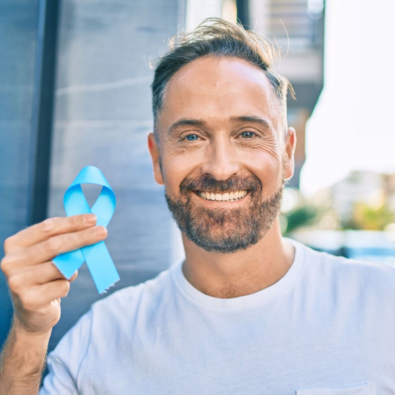 A man with a beard is holding a blue ribbon and smiling.