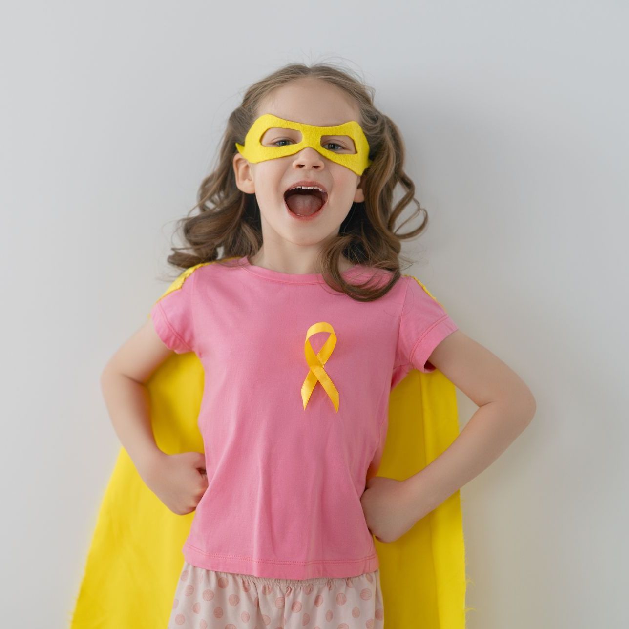 A little girl wearing a pink shirt and a yellow cape