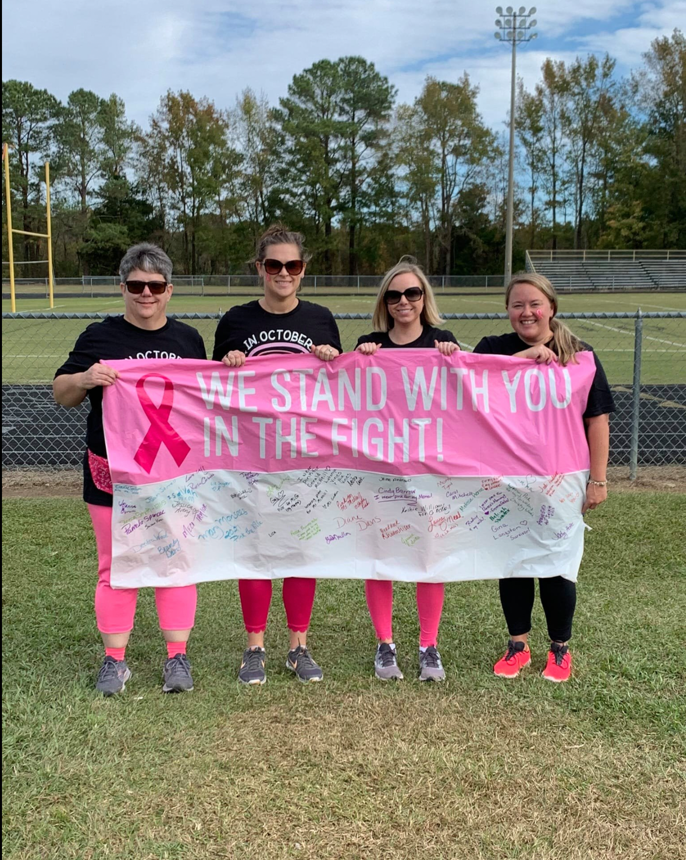 A group of women are holding a pink breast cancer awareness banner.