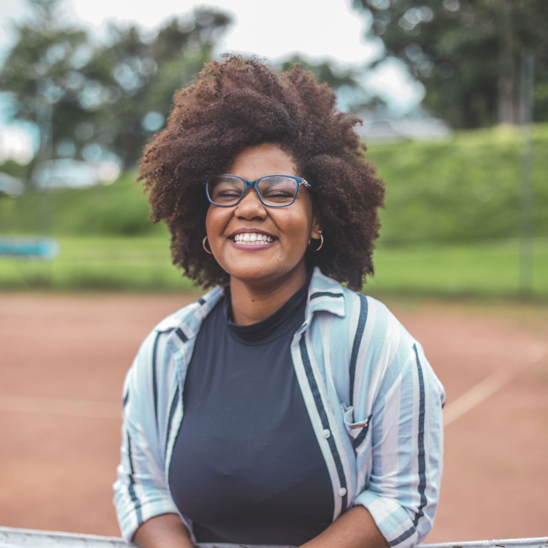 A woman wearing glasses and a black shirt is smiling while sitting on a fence.