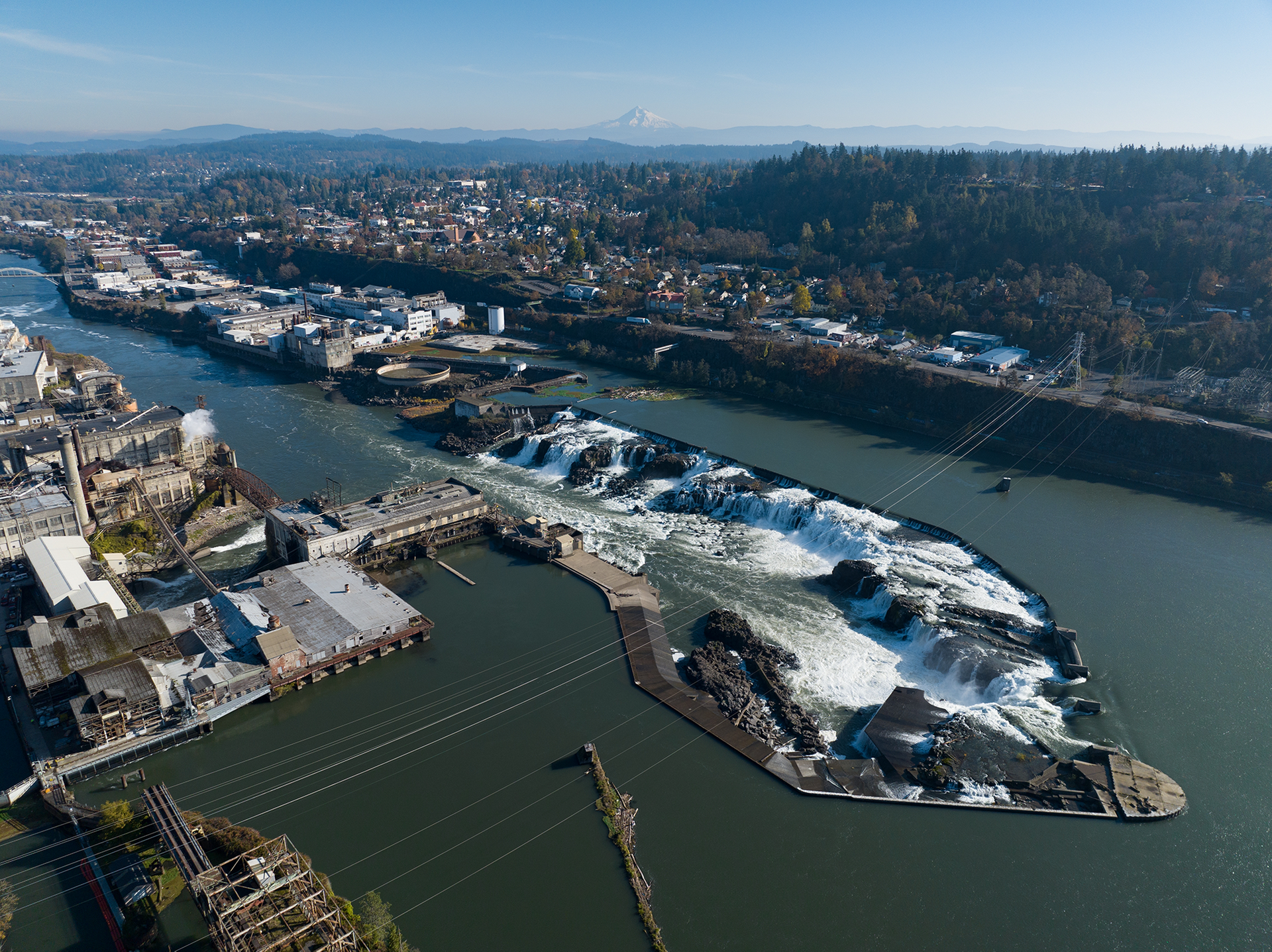 Aerial view of a snowy river and bridge with a city and harbor under a clear sky
