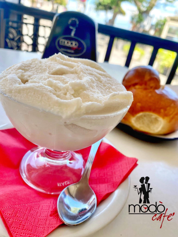 Una coppa di granita in vetro con panna montata, accompagnata da un panino brioche su un tovagliolo rosso al Modò Café.