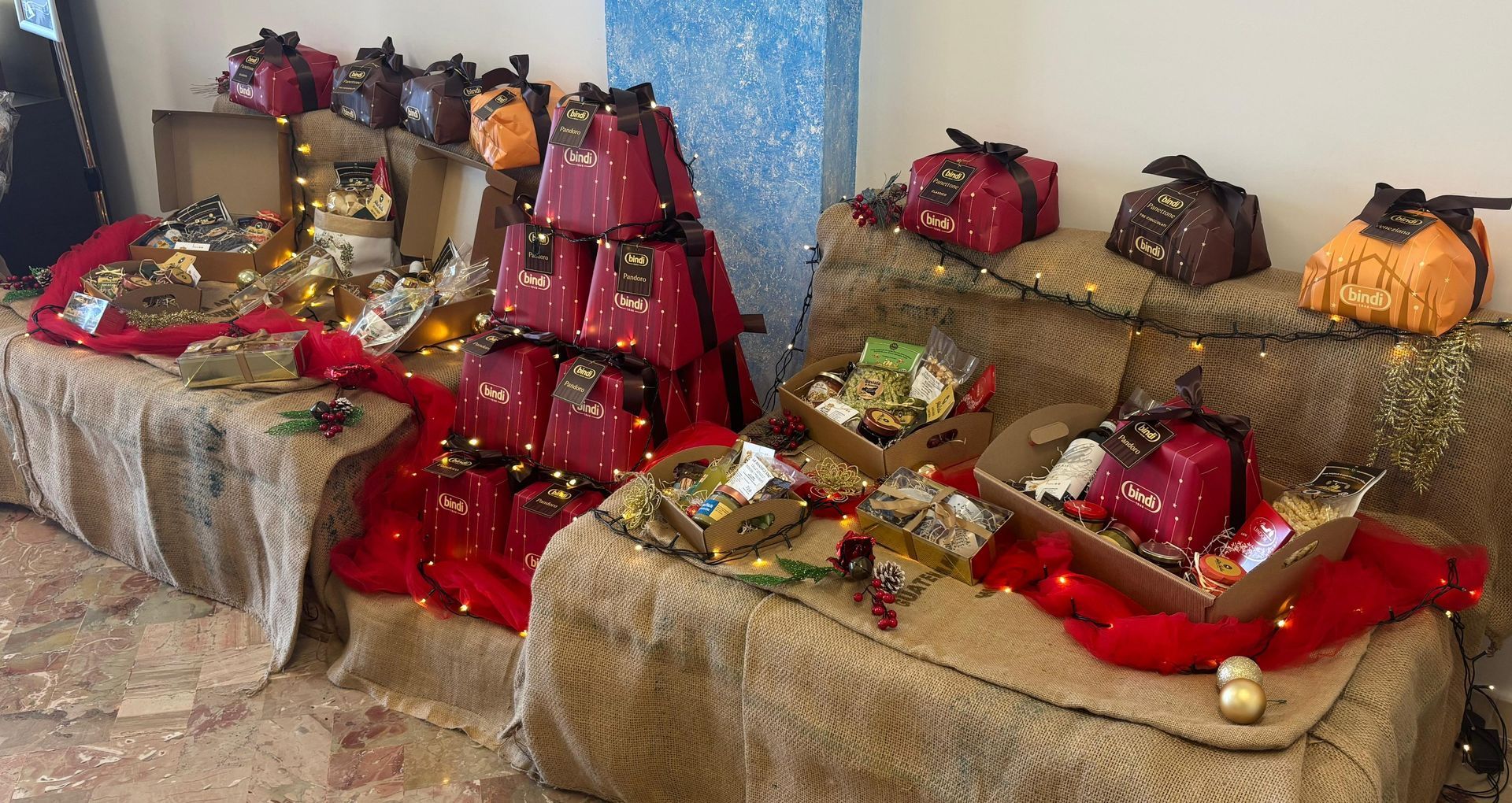 Esposizione di scatole e cesti regalo rossi e arancioni disposti su tavoli ricoperti di tela di iuta e decorati con tessuto rosso.