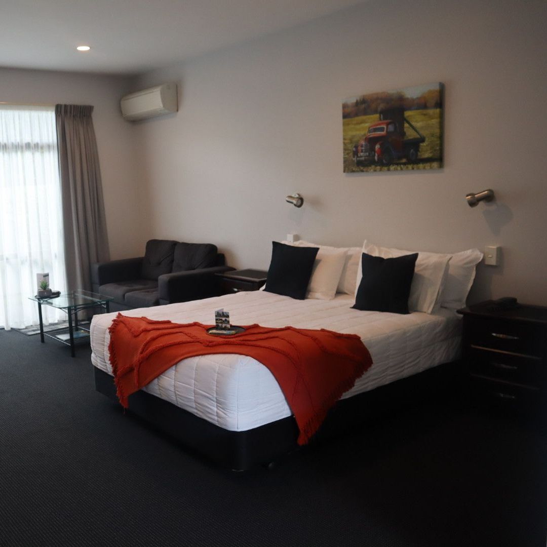 Hotel room with a queen bed, couch, artwork, and curtains.