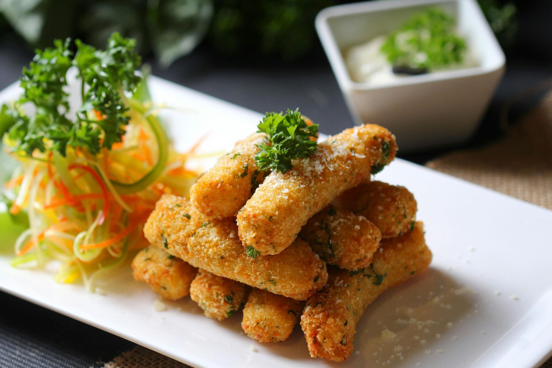 Golden fried mozzarella sticks on a white plate with a side of sauce and salad.