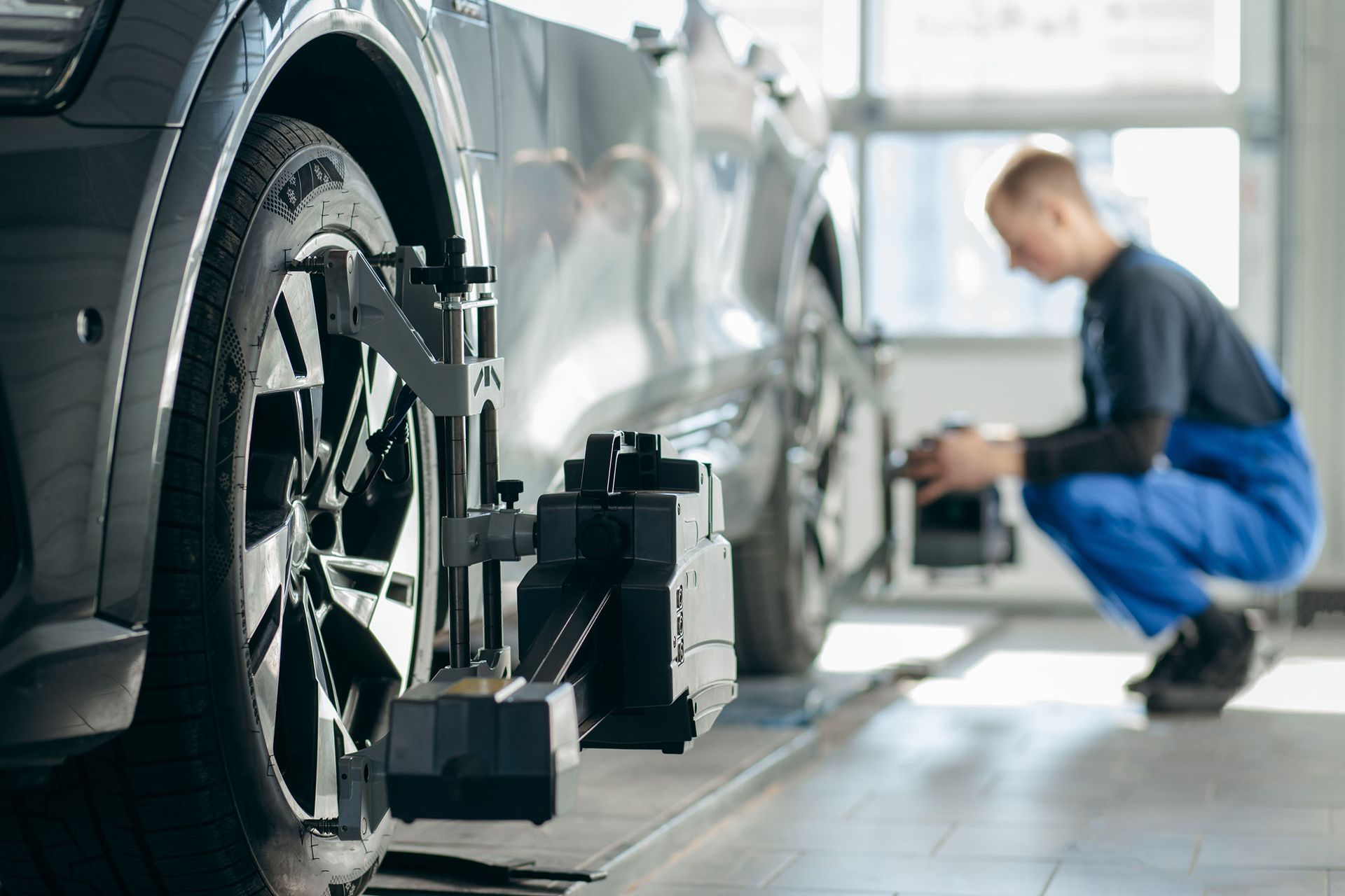 Ein Mann hockt neben einem Auto in einer Garage und montiert ein Achsvermessungsgerät.