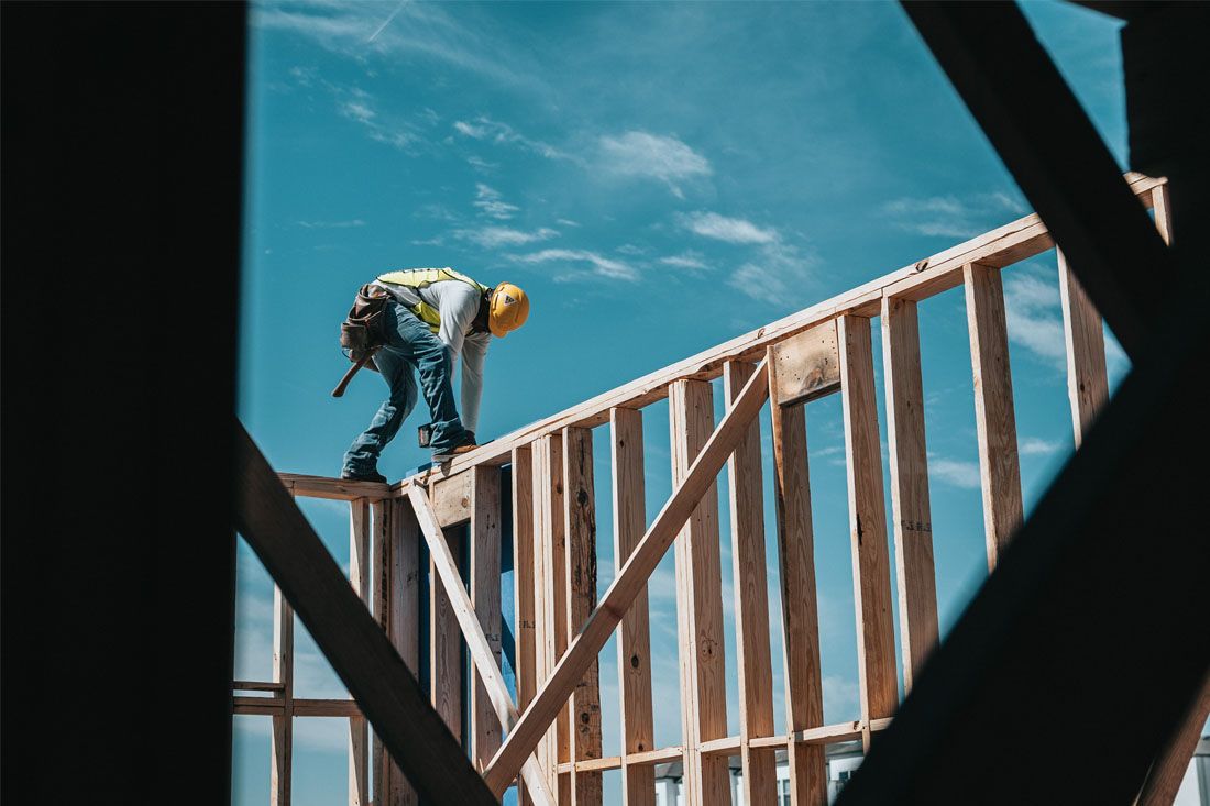 Construction worker bending on a wooden roof frame against a blue sky