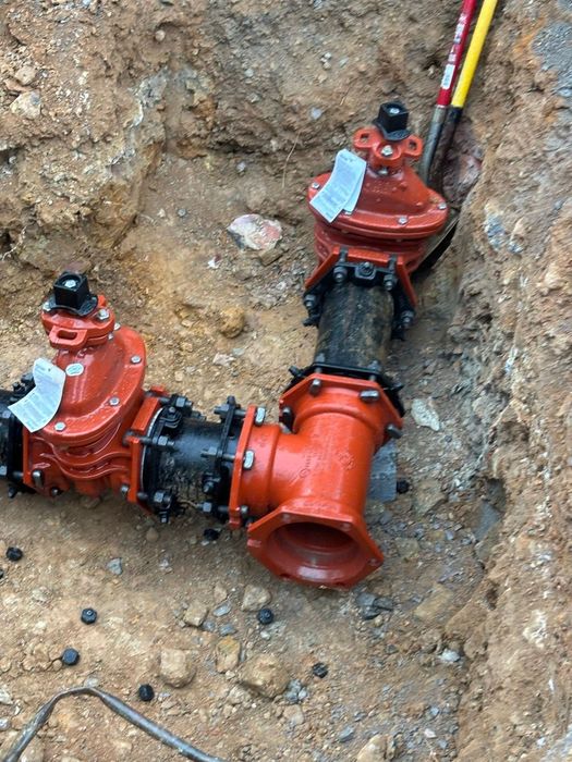 Red fire hydrant valves and black pipe fittings installed in a dirt trench with yellow utility cable nearby