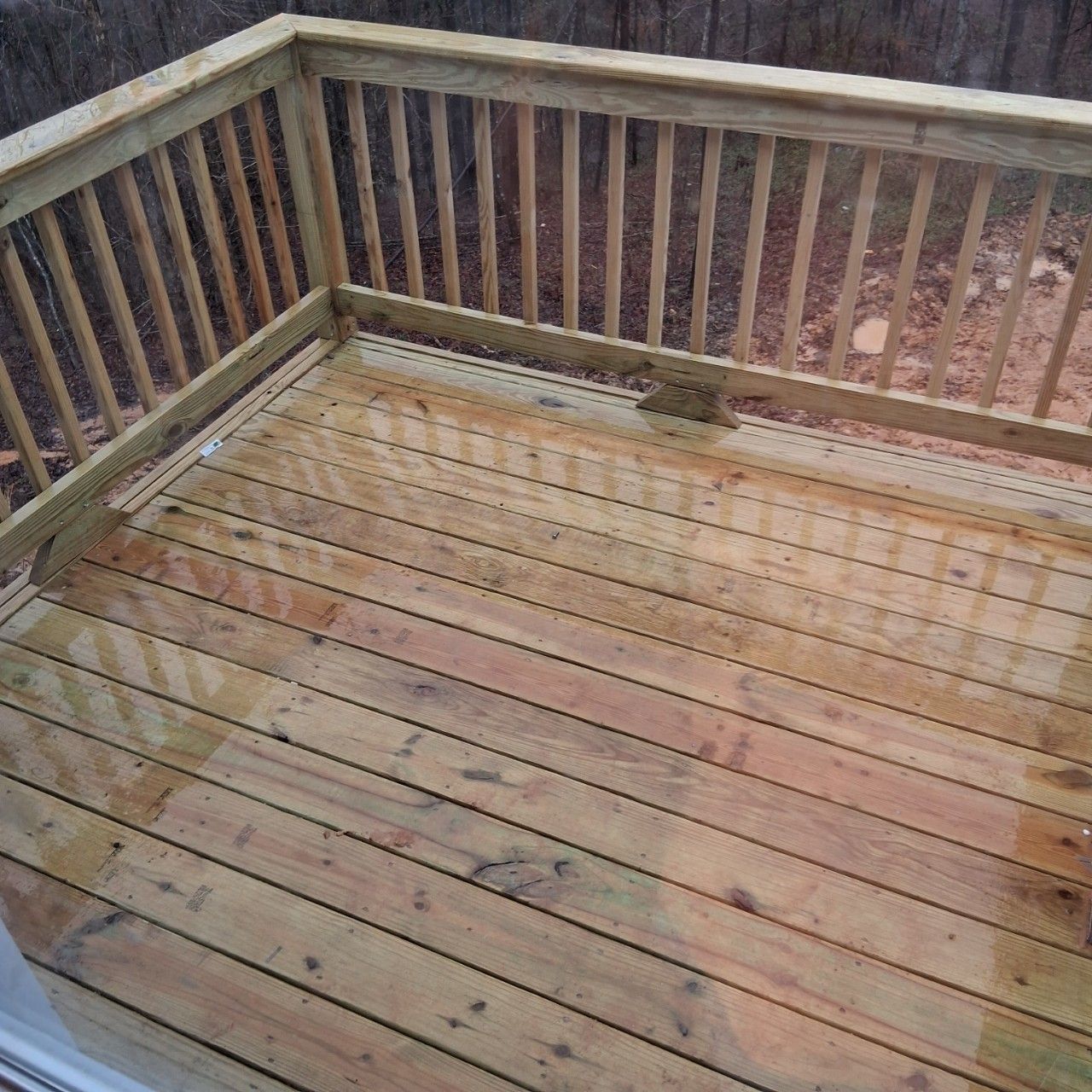 Weathered wooden deck with railings, damp from rain, viewed from a corner.