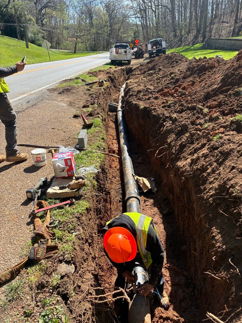 Workers repairing a roadside trench with exposed pipeline beside a rural road
