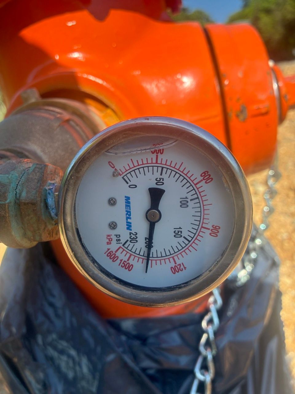Close-up of a pressure gauge on an orange industrial pipe, with a chain attached