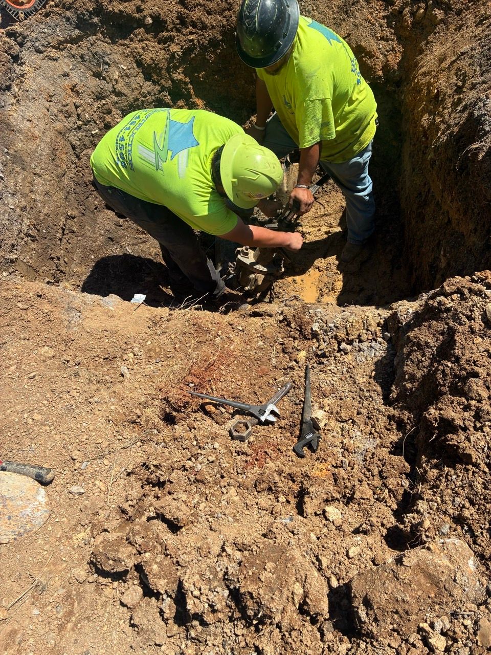 Two workers in neon safety shirts digging in a dirt trench outdoors