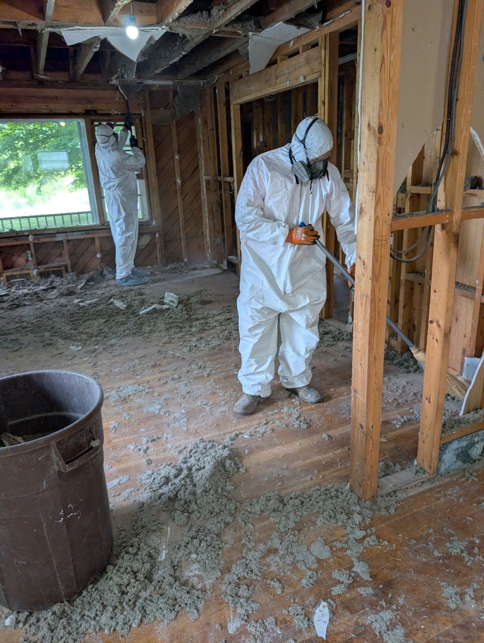 Worker in white protective suit cleaning debris inside a damaged, unfinished room