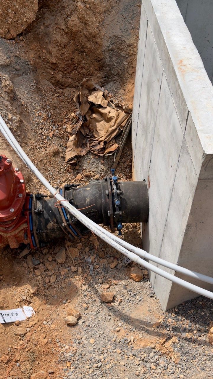 Excavation trench with a black pipe entering a concrete wall beside exposed dirt and debris