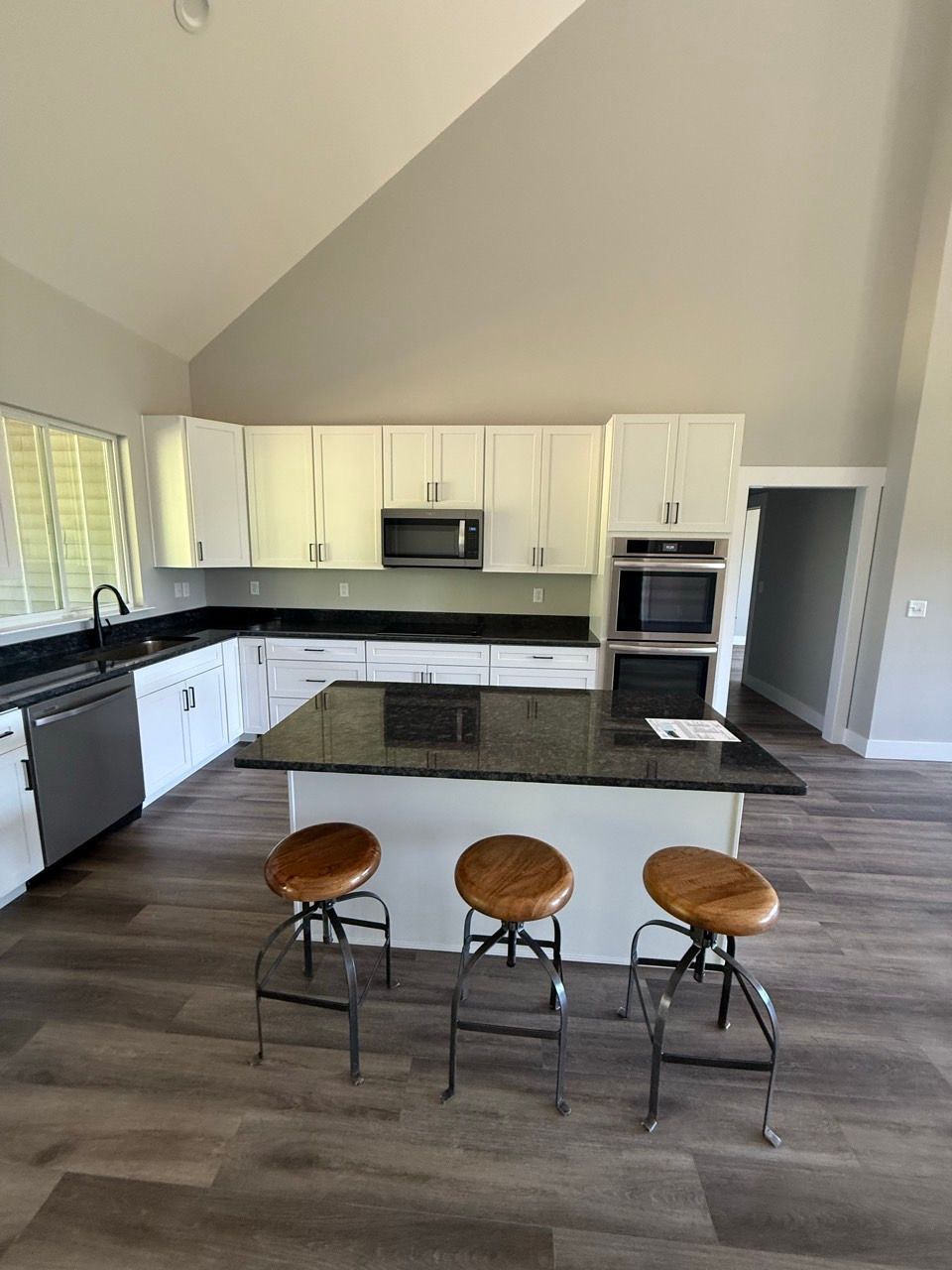 Open kitchen with white cabinets, dark countertops, gray floors, and three stools at a breakfast bar.
