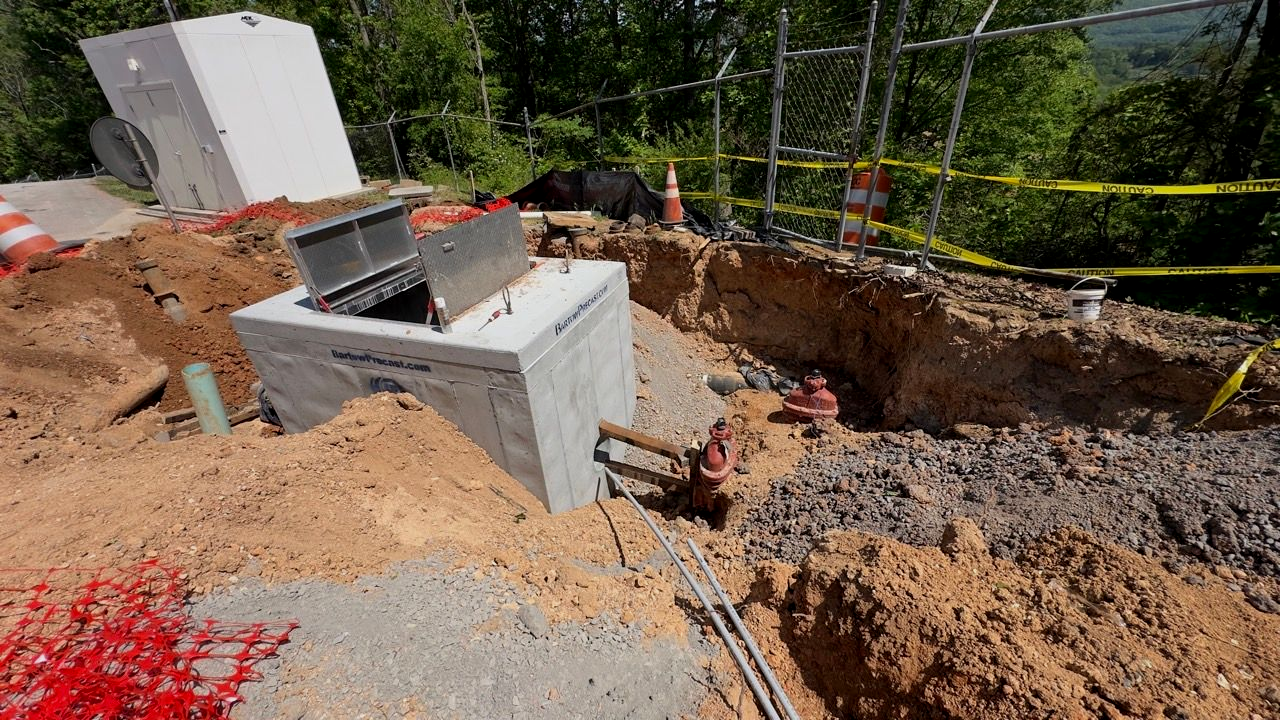 Construction site with excavated trench, concrete foundations, dirt piles, and utility equipment.