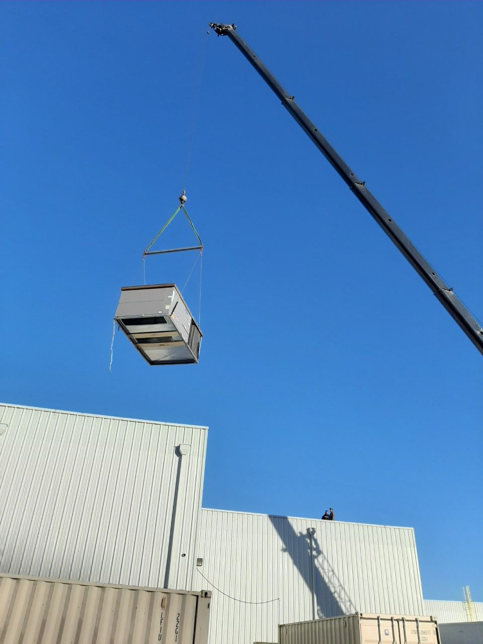 Crane lifting a large crate above a corrugated metal building under a clear blue sky