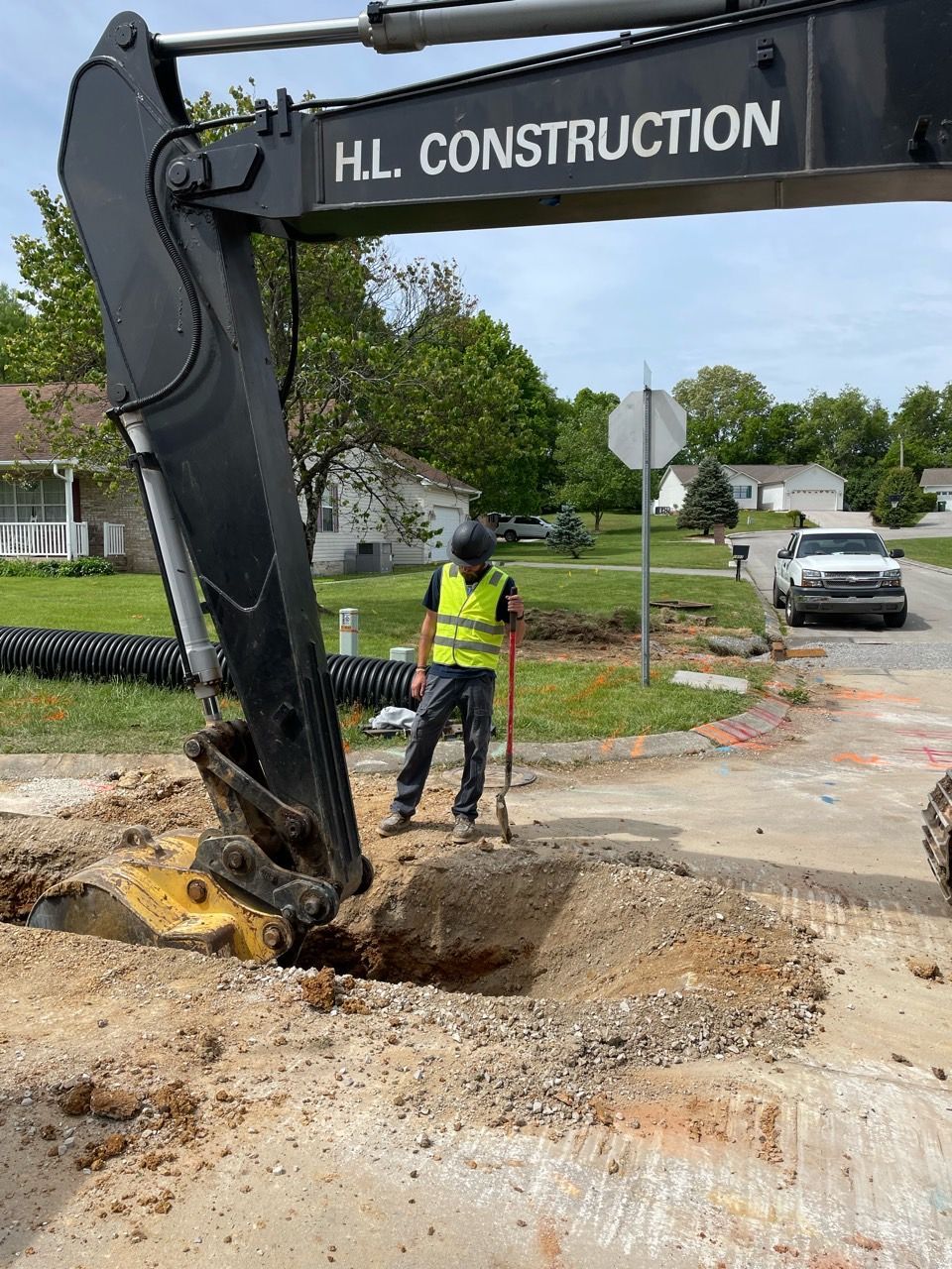 Construction worker beside excavator digging a road trench on a residential street
