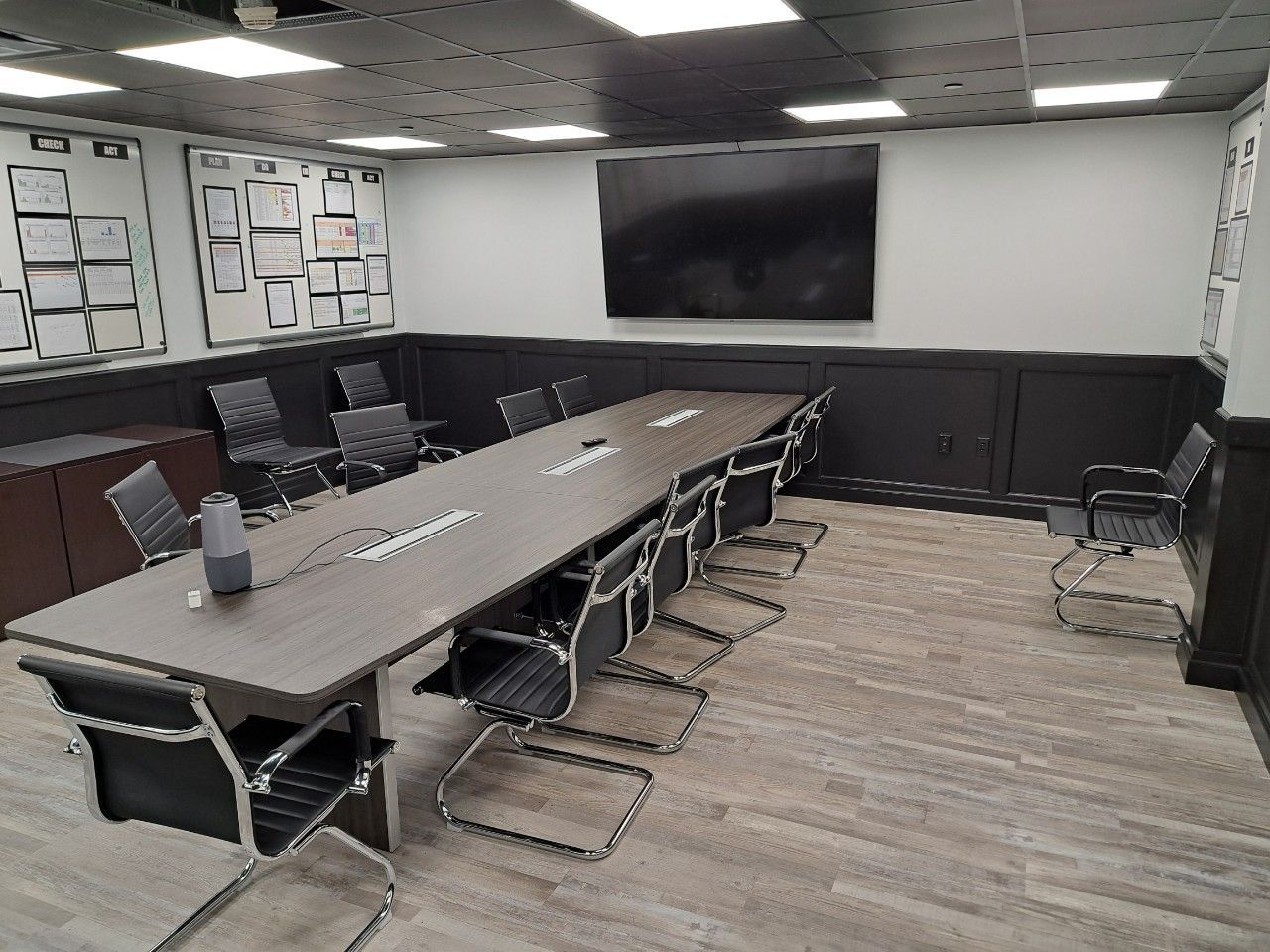 Conference room with long table, black chairs, wall-mounted TV, and patterned ceiling lights.