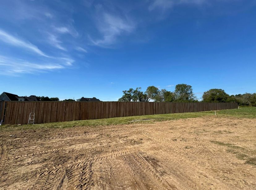 A wooden fence surrounds a dirt field with trees in the background.