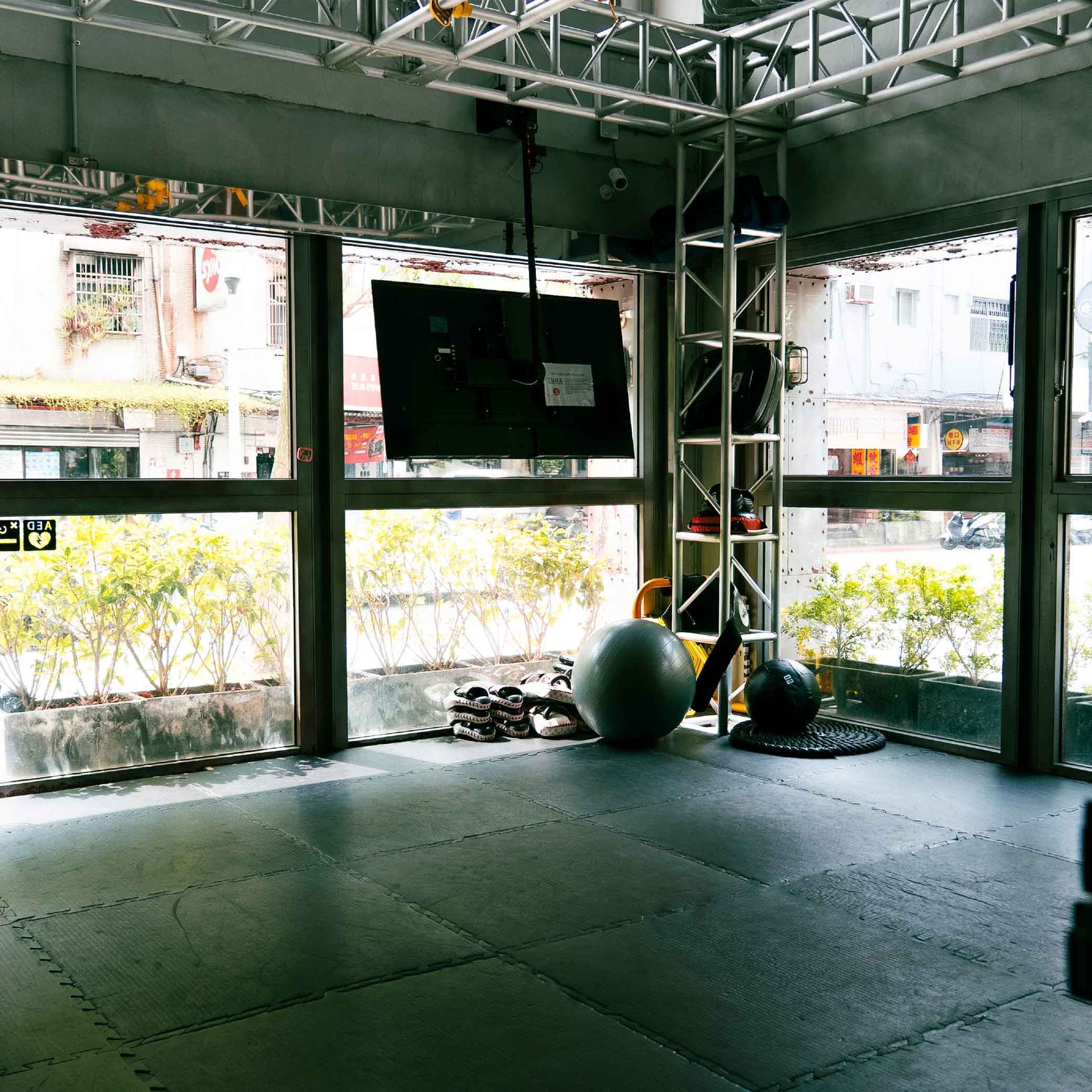 空曠的拳館空間鋪著黑色墊子，有大窗戶，金屬柱旁放著一個藍色健身球。