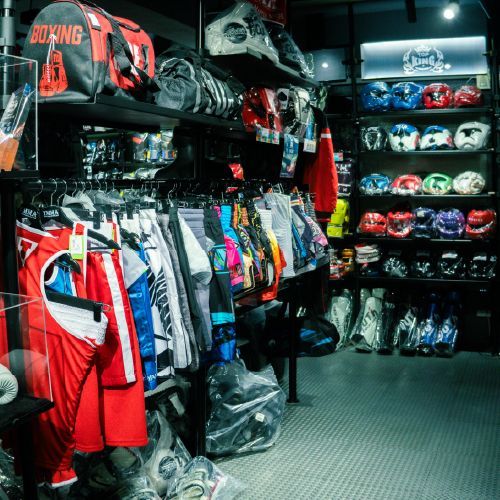 忠孝館商品裝備展售空間，貨架上掛著拳擊服、拳擊手套、各式格鬥裝備和頭盔。