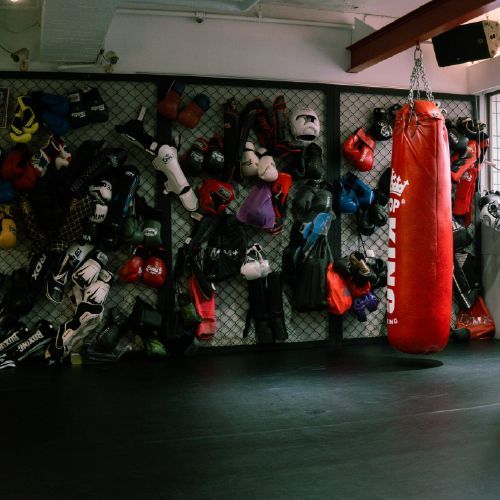 拳館牆上掛著拳擊手套，一個紅色TOPKING沙袋懸掛在牆邊。
