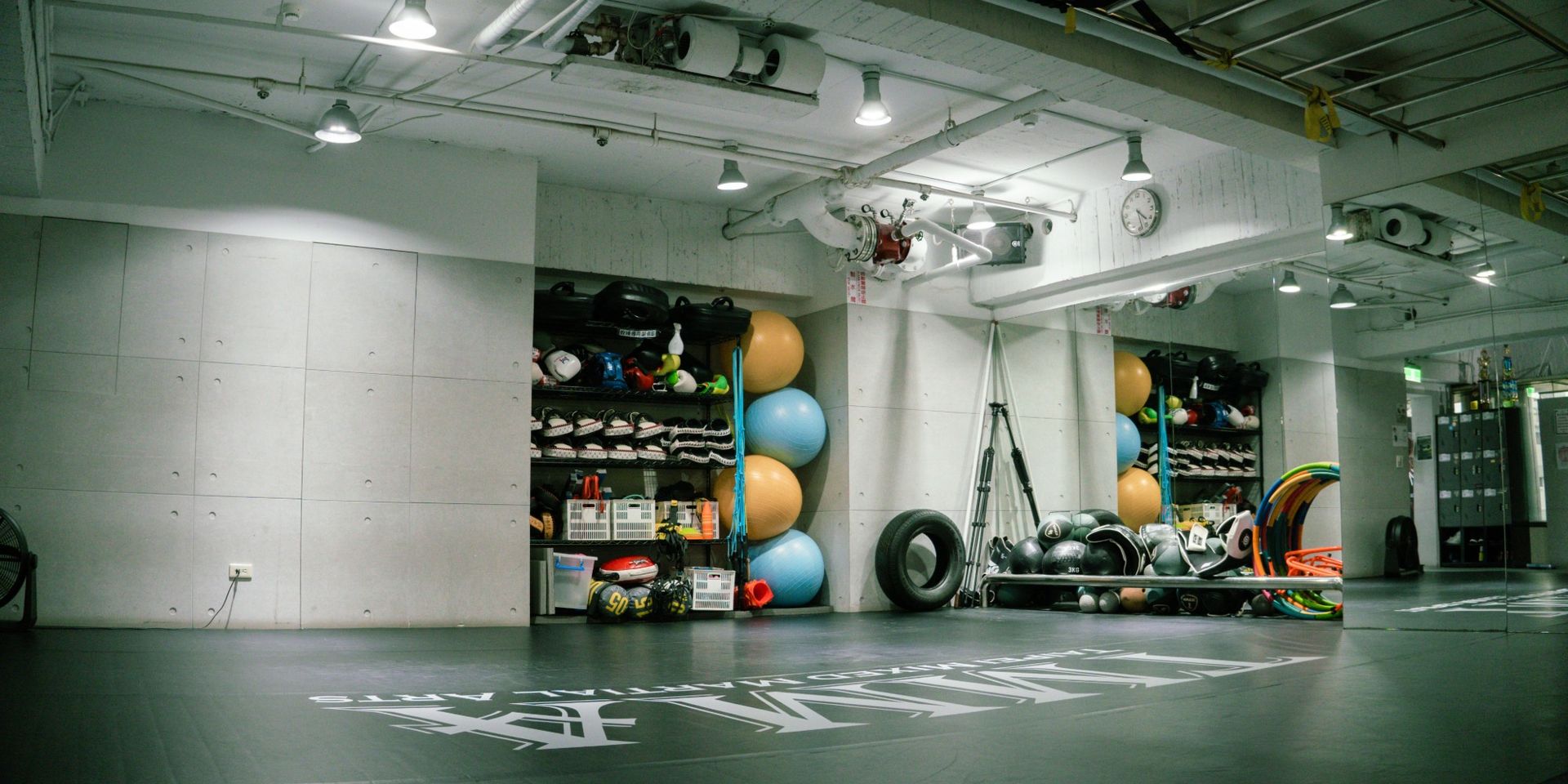 空曠的拳館裡擺放著健身器材、健身球和墊子，頭頂的燈光明亮。